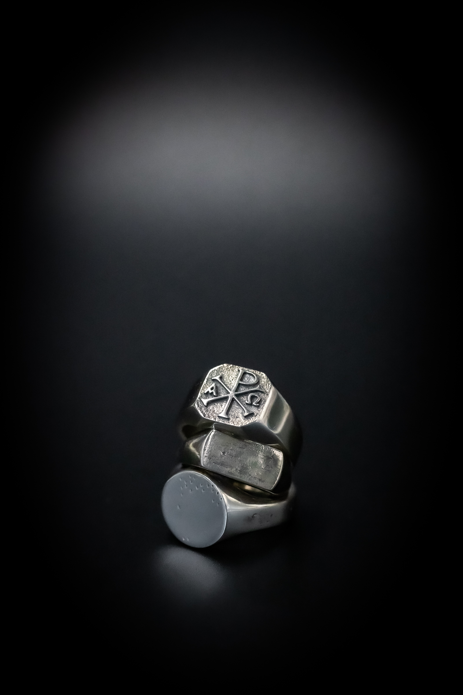 Darma stacked silver signet rings with chi rho engraving on black — product photography by Murrieta Media
